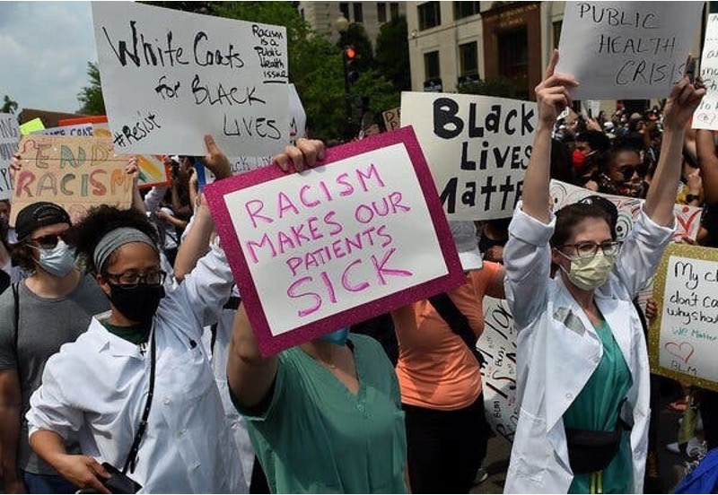 Health workers, some in white laboratory coats and all wearing masks, demonstrating in Washington in 2020. Protesters are holding signs that read: ‘End Racism’, ‘White Coats for Black Lives. Racism is a public health issue’, ‘Racism makes our patients sick’, ‘Black Lives Matter’, and ‘Public Health Crisis’.