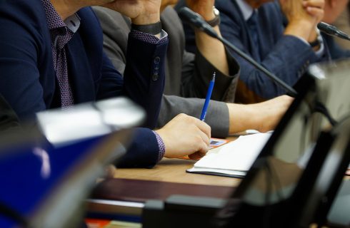 Participants in a business meeting with notebooks, pens, watches
